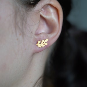 May include: A pair of gold leaf earrings. The earrings are small and delicate, and they feature a simple design of a leaf.