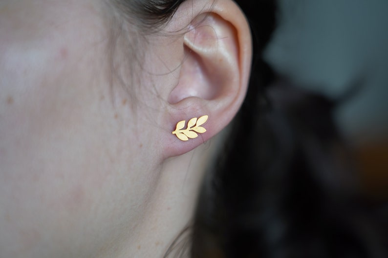 May include: A pair of gold leaf earrings. The earrings are small and delicate, and they feature a simple design of a leaf.
