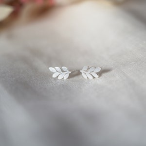 May include: A pair of silver leaf earrings. The earrings are small and delicate, and they have a simple, elegant design.