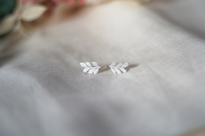 May include: A pair of silver leaf earrings. The earrings are small and delicate, and they have a simple, elegant design.