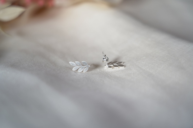May include: A pair of silver leaf earrings. The earrings are in the shape of a branch with multiple leaves.