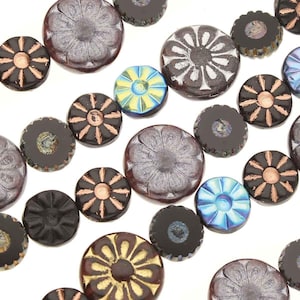 May include: A selection of glass beads in brown, black, blue, and gold. The beads have floral and geometric patterns, with some having a textured or scalloped edge. The round beads appear to be handmade, suitable for jewellery making or crafts.