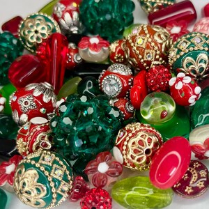May include: A collection of red, green, and gold glass beads with intricate designs. The beads are perfect for jewelry making or crafting.