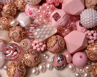 May include: A collection of pink and white beads with gold accents. The beads are made of various materials, including wood, glass, and metal. Some of the beads have intricate designs, while others are plain. The beads are perfect for making jewelry or other crafts.