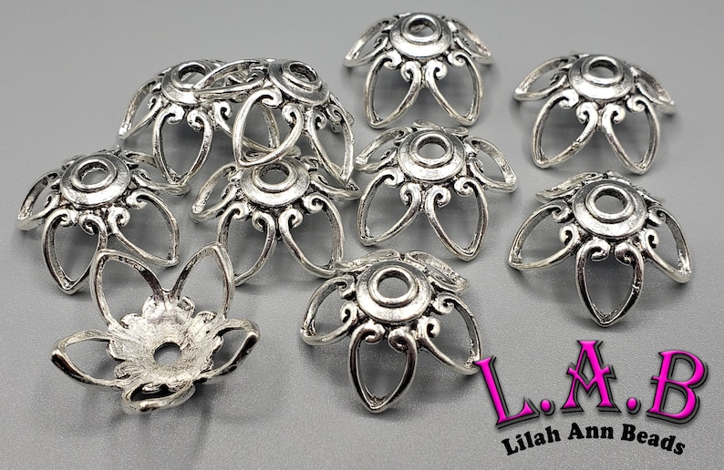 K&ouml;nnte beinhalten: Silberfarbene Metallperlenkappen mit floralem Design. Die Kappen haben ein zentrales Loch und sind von stilisierten Bl&uuml;tenbl&auml;ttern umgeben. Das Bild enth&auml;lt den Text "L.A.B Lilah Ann Beads".