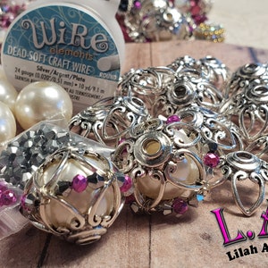 May include: An assortment of jewelry-making supplies, including silver-colored filigree bead caps, faux pearls, and small bags of crystals in various colors. A spool of wire is also visible, with the text "Wire elements DEAD-SOFT CRAFT WIRE". The text "L.A.B Lilah Ann Beads" is also visible.