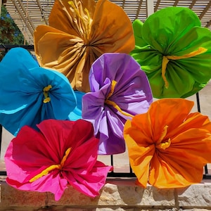 K&ouml;nnte beinhalten: Eine Ansammlung von sechs gro&szlig;en, handgefertigten Papierblumen in leuchtenden Farben wie Gold, Limettengr&uuml;n, Hellblau, Lavendel, Pink und Orange. Jede Blume hat eine geraffte Mitte mit einem gelben Detail und wellenf&ouml;rmigen Bl&uuml;tenbl&auml;ttern.