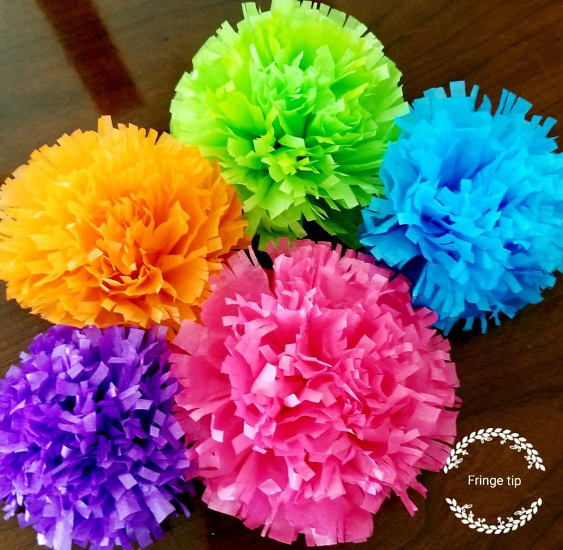 Pu&ograve; includere: Sei pompon di carta velina dai colori vivaci: arancione, verde, blu, rosa, viola e giallo. I pompon sono disposti in un motivo circolare, ognuno con un bordo sfrangiato. Il testo "Fringe tip" &egrave; visibile in basso a destra.