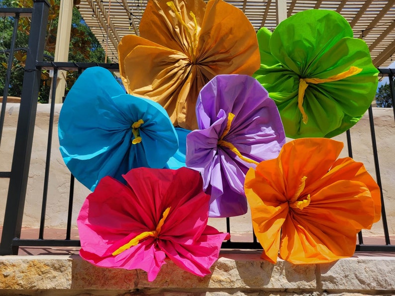 K&ouml;nnte beinhalten: Eine Ansammlung von sechs gro&szlig;en, handgefertigten Papierblumen in leuchtenden Farben wie Gold, Limettengr&uuml;n, Hellblau, Lavendel, Pink und Orange. Jede Blume hat eine geraffte Mitte mit einem gelben Detail und wellenf&ouml;rmigen Bl&uuml;tenbl&auml;ttern.