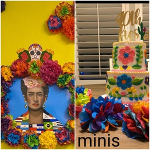 Pu&ograve; includere: Immagine vibrante con un ritratto di Frida Kahlo circondato da fiori di carta colorati e un teschio di zucchero. &Egrave; presente anche una torta a tre piani con decorazioni floreali e un topper "40th Fiesta", insieme ad altri fiori di carta. La parola "minis" &egrave; in basso.
