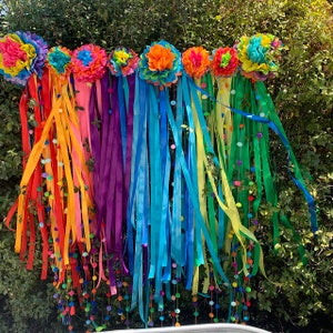 May include: A vibrant, rainbow-colored garland featuring colorful paper flowers and long, flowing ribbons. The garland is adorned with confetti and small, decorative balls, creating a festive and eye-catching display. Perfect for parties or celebrations.
