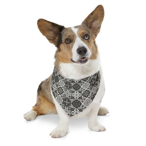 Op de afbeelding: Een driekleurige Corgi-hond met een zwart-wit patroon bandana. De bandana heeft een herhalend bloemen- en geometrisch ontwerp. De hond heeft één blauw oog en één bruin oog en zit op een witte achtergrond.