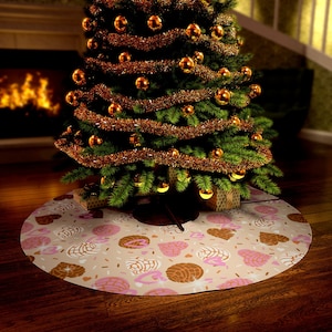 Op de afbeelding: Een ronde kerstboomrok met een beige achtergrond en een patroon van concha-brood in bruin, roze en wit. De rok ligt onder een versierde kerstboom met gouden ballen en slingers.