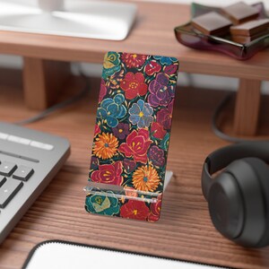 May include: A floral patterned phone stand featuring a vibrant array of red, blue, purple, and orange flowers on a dark background. The stand is made of a sturdy material and is designed to hold a phone upright.