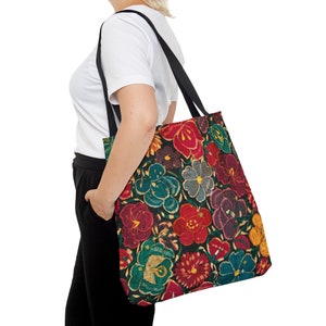 May include: A tote bag with a vibrant floral pattern in red, teal, yellow, and purple on a black background. The bag has black straps and is carried over the shoulder. The floral design is detailed and eye-catching.