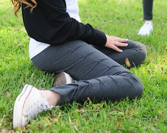 Può includere: Una persona con pantaloni della tuta grigi e scarpe da ginnastica bianche è seduta su un prato.