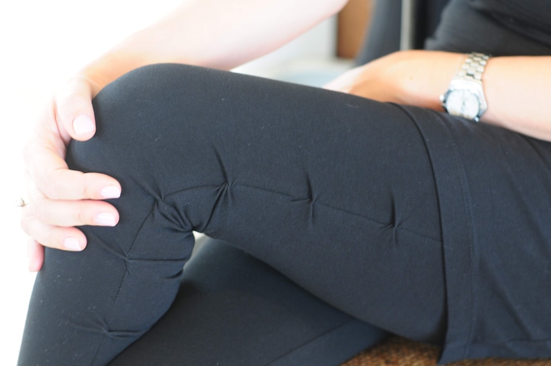 May include: A close-up of a person wearing black leggings with a seam detail on the legs. The person is wearing a watch on their wrist.