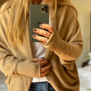 May include: A tan cardigan with long sleeves and a draped front. The cardigan is made of a soft, comfortable fabric and has a relaxed fit.