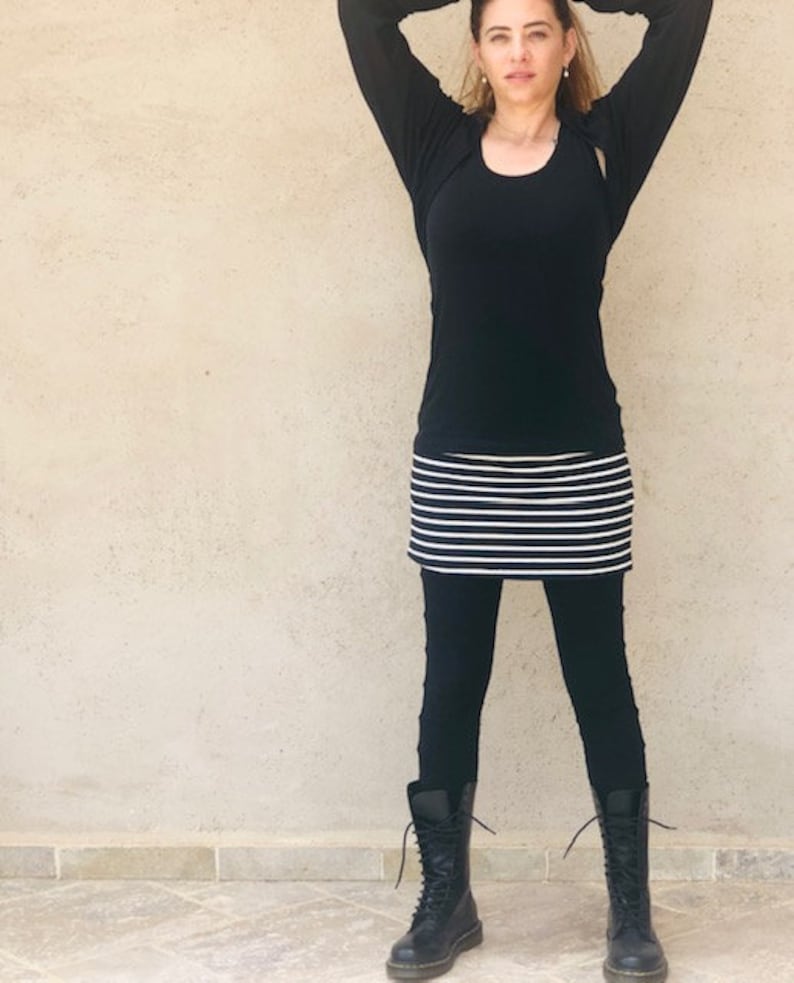 Pu&ograve; includere: Una donna indossa una camicia nera a maniche lunghe, una gonna a righe bianche e nere e stivali neri da combattimento.