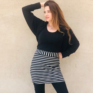 Pu&ograve; includere: Una gonna a righe bianche e nere con una maglia nera e un cardigan nero. La donna indossa leggings neri.