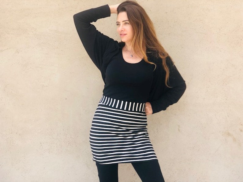 Pu&ograve; includere: Una gonna a righe bianche e nere con una maglia nera e un cardigan nero. La donna indossa leggings neri.