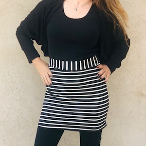 Pu&ograve; includere: Una gonna a righe bianche e nere con una maglia nera e un cardigan nero. La gonna ha una cintura larga.