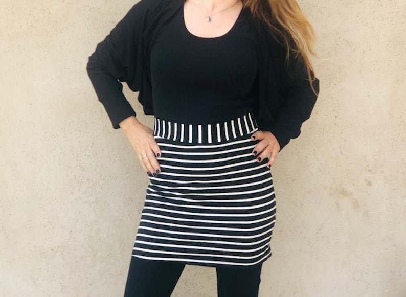 Pu&ograve; includere: Una gonna a righe bianche e nere con una maglia nera e un cardigan nero. La gonna ha una cintura larga.