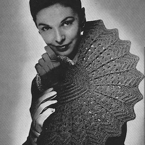 Puede incluir: Un bolso de crochet negro con un diseño en forma de abanico. El bolso está siendo sostenido por una persona que lleva una blusa oscura y guantes.