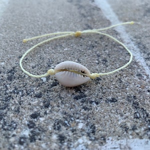 May include: A simple white shell bracelet with a light yellow cord.