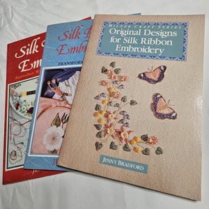 May include: Three books on silk ribbon embroidery. The book on the right has the title "Original Designs for Silk Ribbon Embroidery" with butterfly and floral illustrations. The other books have titles "Silk Embroidery" and "Silk Embroidery: Transforming".