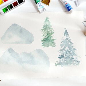 May include: Watercolour painting of mountains and evergreen trees in shades of blue and green. The artwork is on a large sheet of paper, surrounded by tubes of paint, a watercolour palette, and paintbrushes. The art supplies are arranged on a white surface.