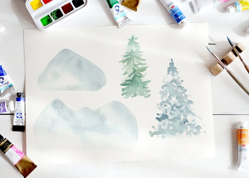 May include: Watercolour painting of mountains and evergreen trees in shades of blue and green. The artwork is on a large sheet of paper, surrounded by tubes of paint, a watercolour palette, and paintbrushes. The art supplies are arranged on a white surface.