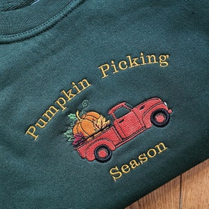 May include: A green sweatshirt with embroidered text that reads "Pumpkin Picking Season" and a red truck with a pumpkin in the back.