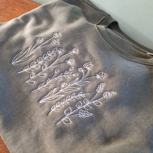 Op de afbeelding: Een groen T-shirt met witte geborduurde bloemen.