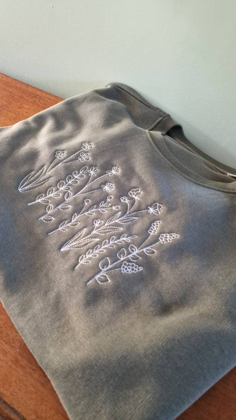 Op de afbeelding: Een groen T-shirt met witte geborduurde bloemen.