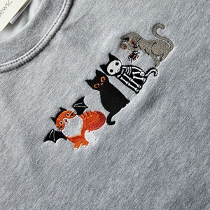 May include: A gray sweatshirt with embroidered black and orange cats. The cats are wearing costumes, including a skeleton costume and a bat costume.