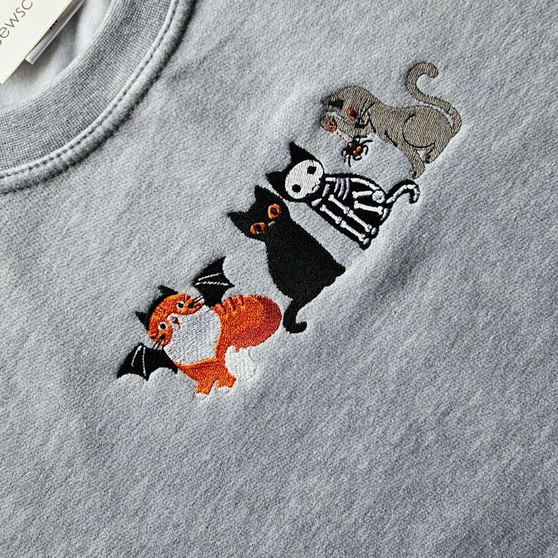 May include: A gray sweatshirt with embroidered black and orange cats. The cats are wearing costumes, including a skeleton costume and a bat costume.