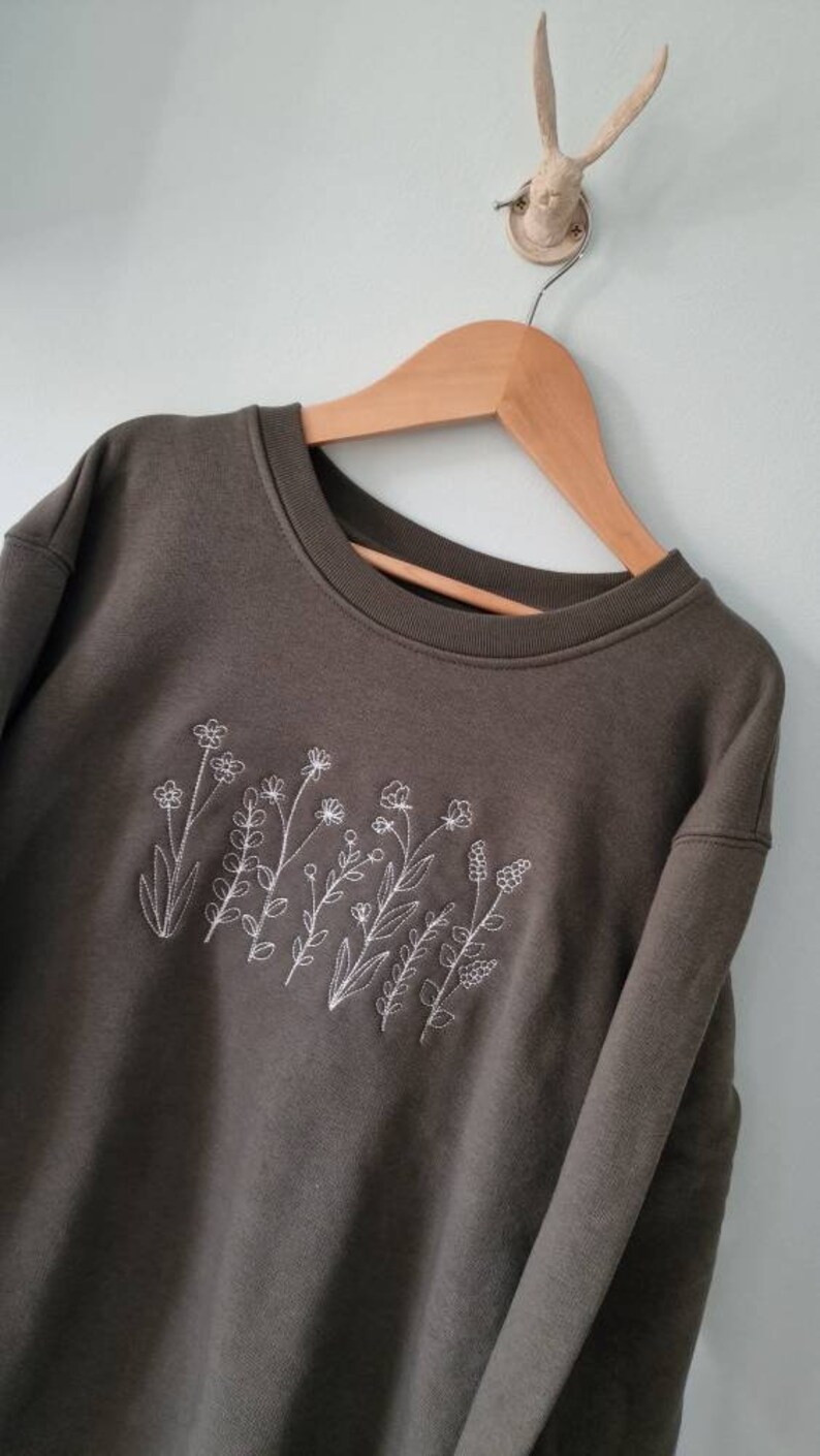 Op de afbeelding: Een donkergroen sweatshirt met een wit geborduurd ontwerp van wilde bloemen.
