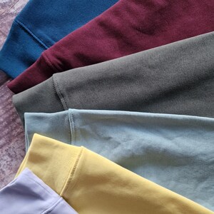 Op de afbeelding: Een stapel van zes stofstalen in verschillende kleuren, waaronder lichtblauw, bordeauxrood, donkergroen, lichtblauw, geel en lichtgrijs.