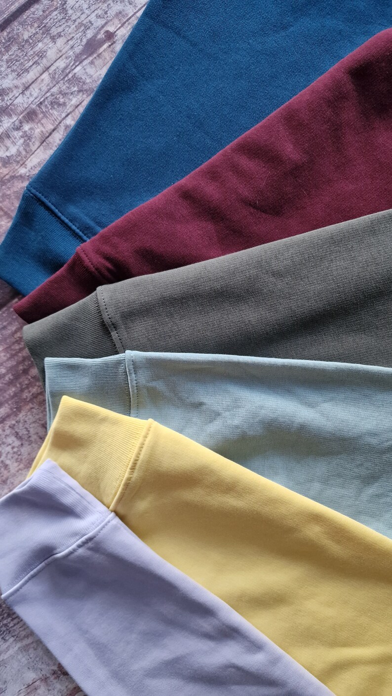 Op de afbeelding: Een stapel van zes stofstalen in verschillende kleuren, waaronder lichtblauw, bordeauxrood, donkergroen, lichtblauw, geel en lichtgrijs.