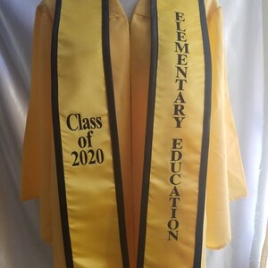 May include: Yellow graduation sash with black trim. The sash has the text "Class of 2020" on one side and "Elementary Education" on the other side.