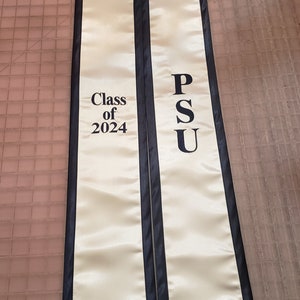 Może przedstawiać: Biała szarfa absolwentka z czarnym wykończeniem. Na szarfie widnieje napis "Class of 2024" po jednej stronie i "PSU" po drugiej.