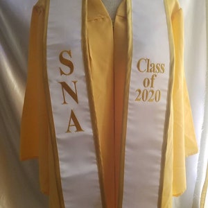Może przedstawiać: Biała szarfa absolwentka z złotymi lam&oacute;wkami i napisem "SNA" po jednej stronie i "Class of 2020" po drugiej.