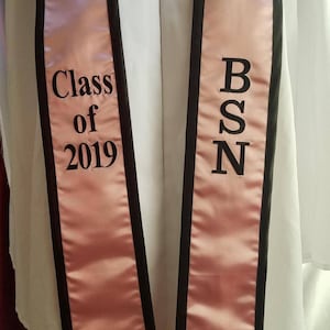 May include: A pink and black graduation sash with the text "Class of 2019" on one side and "BSN" on the other side.