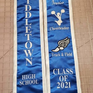 May include: Blue and white graduation sash with white text that reads "Middletown High School" on the left side and "Brielle Lena Frasier Cheerleader Track & Field Class of 2021" on the right side.