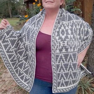 May include: A grey and white crocheted shawl with a geometric pattern. The shawl is being worn by a person with a burgundy tank top and blue jeans.