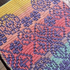 May include: A handmade crochet blanket with a geometric pattern. The blanket features a combination of colors, including yellow, pink, purple, and green. The intricate design showcases a variety of textures and stitch patterns, creating a visually appealing textile.
