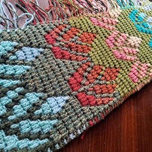 May include: A multi-colored crocheted scarf with a fringe. The scarf is made with different colored yarn in a geometric pattern. The colors include green, blue, red, orange, and pink.