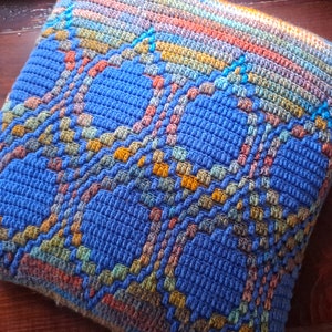 May include: A blue, orange, and yellow crocheted pillow with a geometric pattern.
