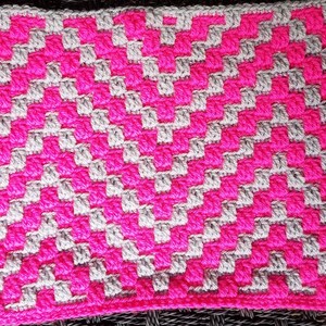 May include: A crocheted blanket with a geometric pattern in pink and gray.